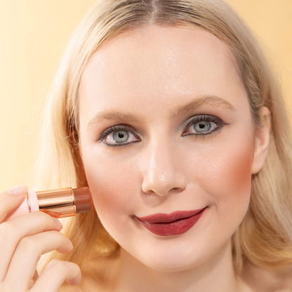 A woman showcasing and wearing on her cheek Oplenza highly pigmented, bold color Blush Stick-Calm