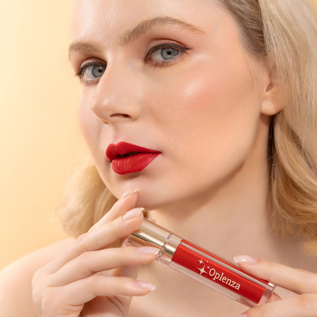 Woman with red lipstick holding a red and gold lip gloss with 'Oplenna' branding. Infinite Flame