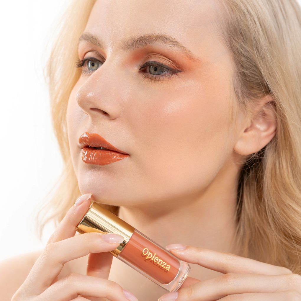 A woman wearing and showcasing the best cruelty-free, vegan, shiny and hydrating lip gloss in shade Sienna